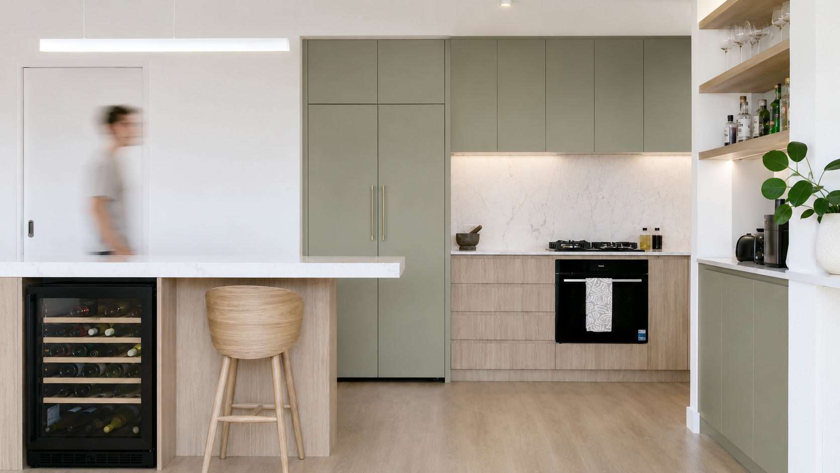 A kitchen with sage-green cabinetry, a marble splashback and a timber island with an integrated wine fridge.