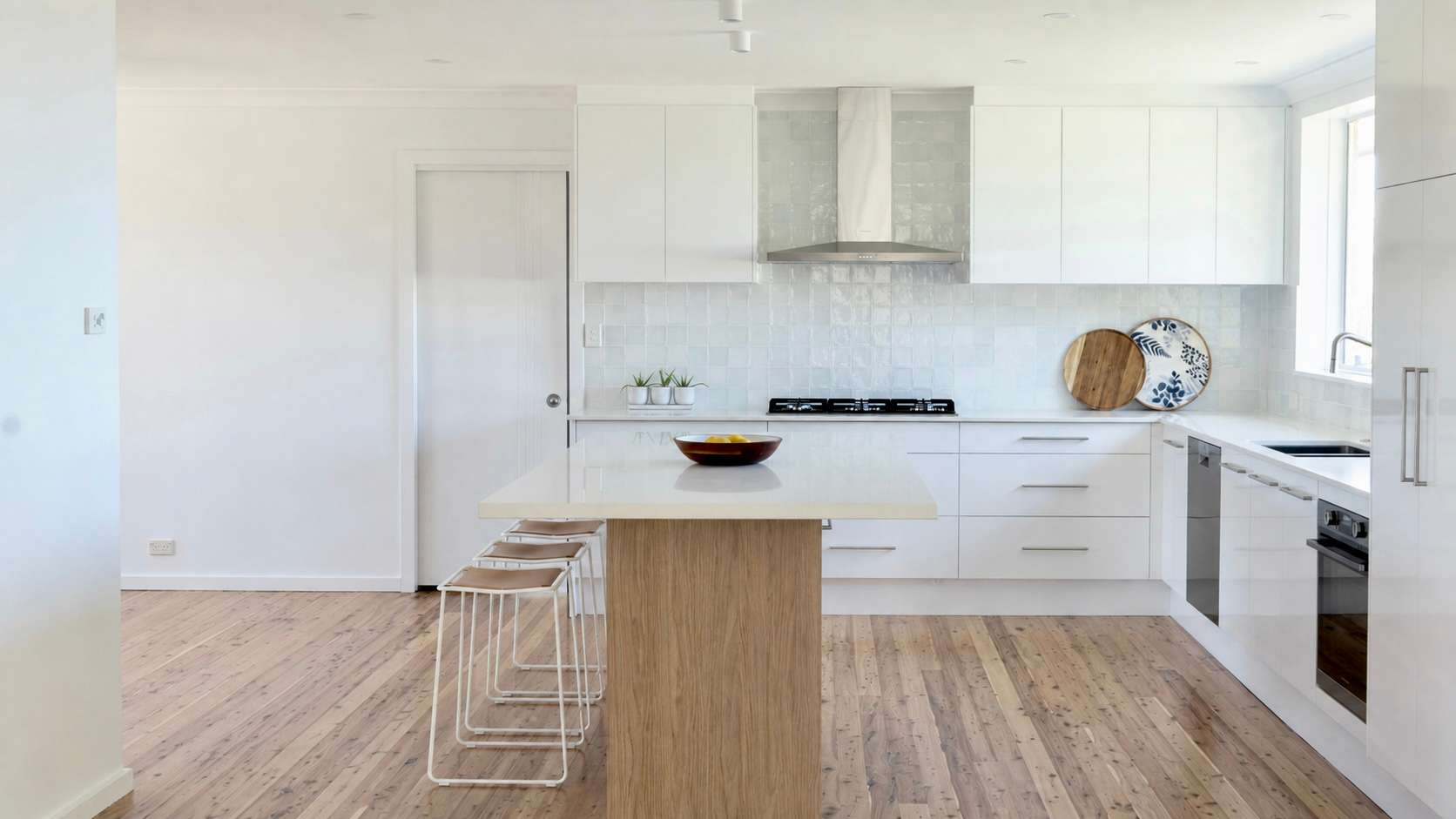 A bright white kitchen with a timber island, bar stools and timber floors.
